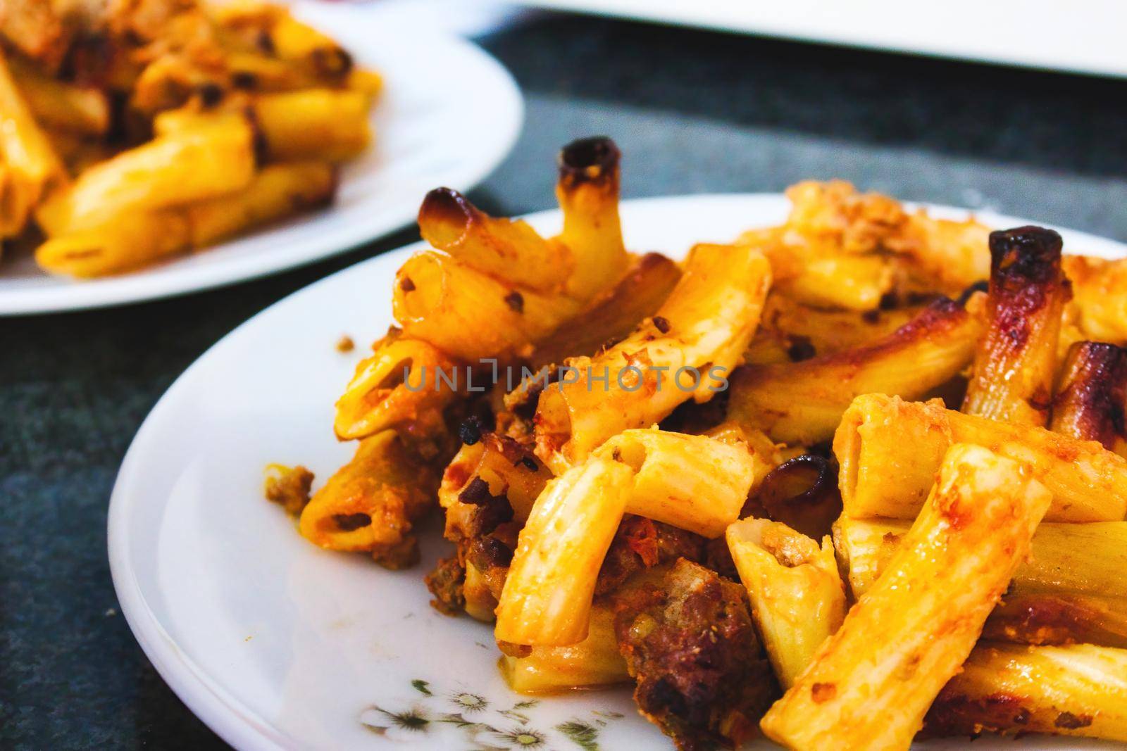 Penne pasta tubes with bolognese sauce on a white plate on a kitchen worktop