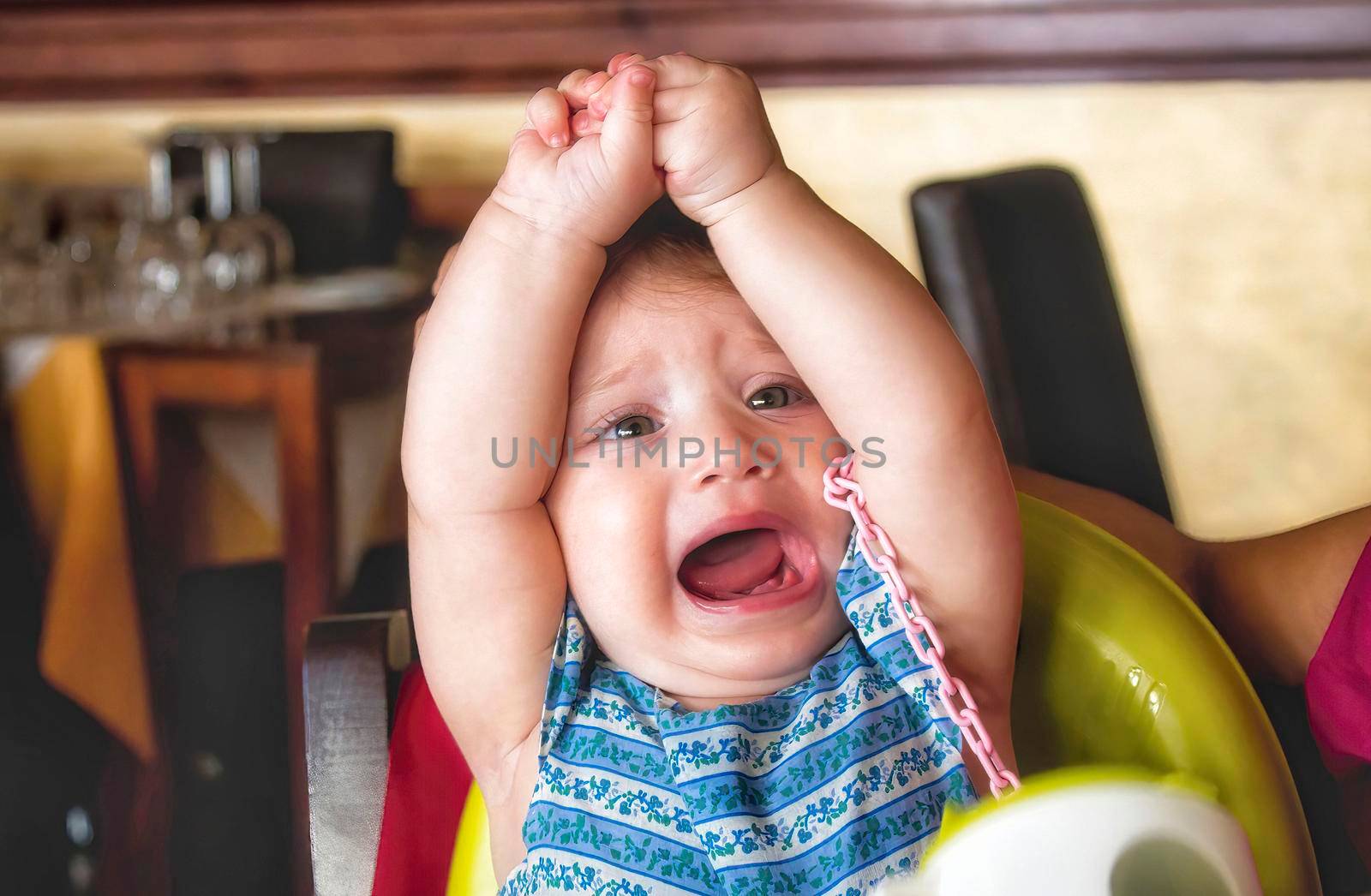 Young child throwing a tantrum in her high chair in a restaurant by tennesseewitney