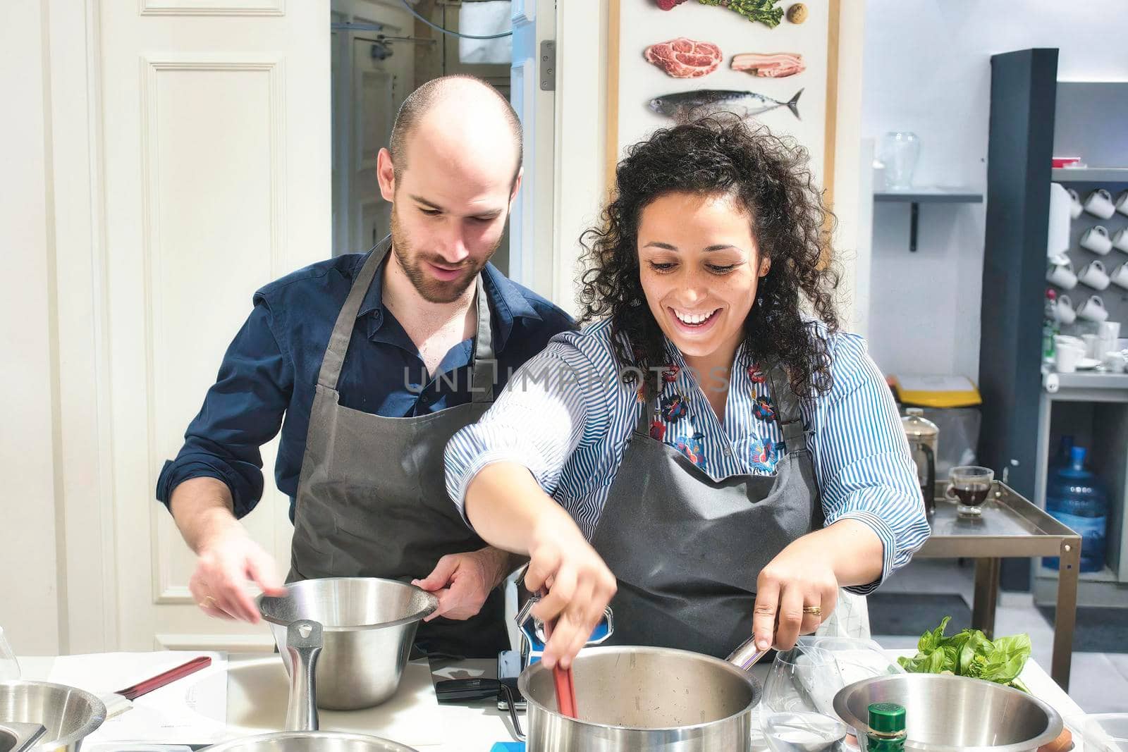 A young couple enjoying cooking together in the kitchen wearing aprons by tennesseewitney