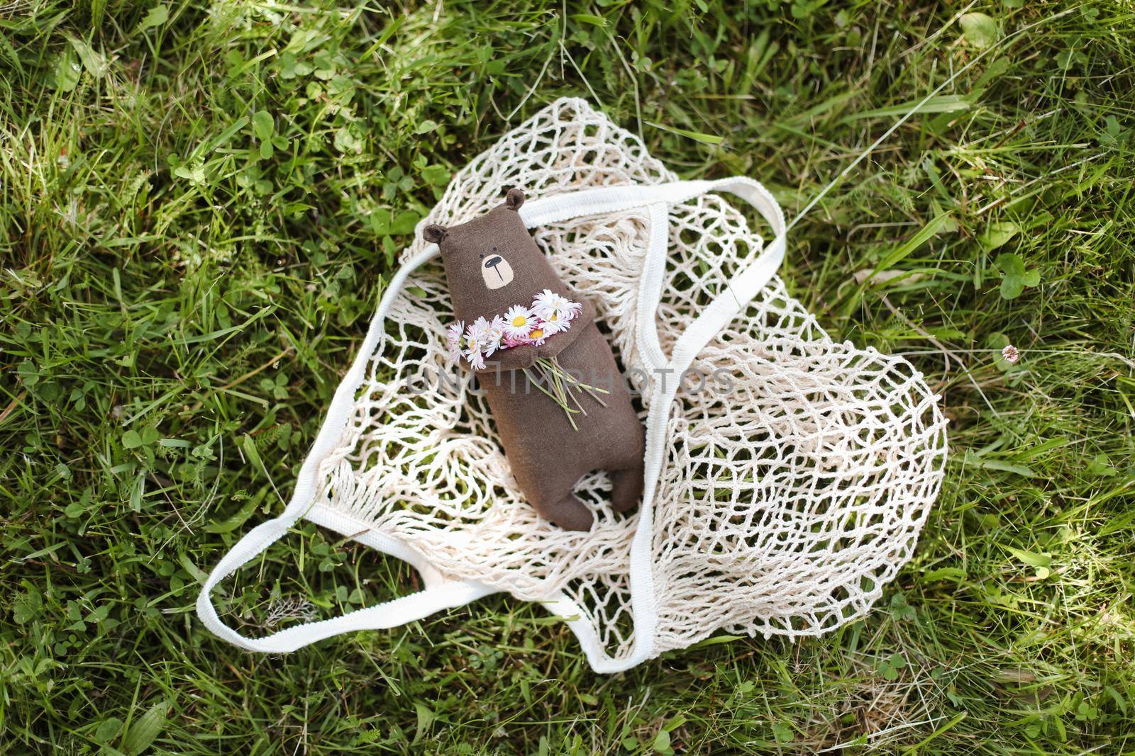 Eco-friendly cute handmade toy bear on grass at sunny summer day