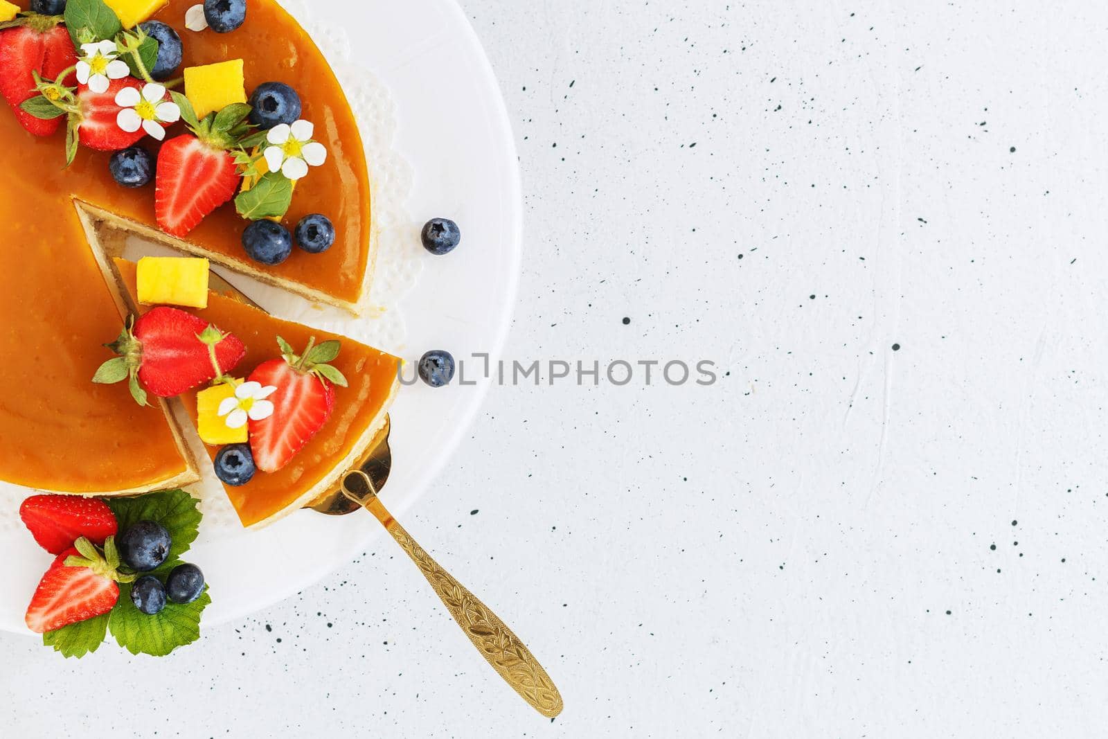 A piece of sliced mango cheesecake on a stand, garnished with berries and flowers. Healthy dessert. Vegetarian food.