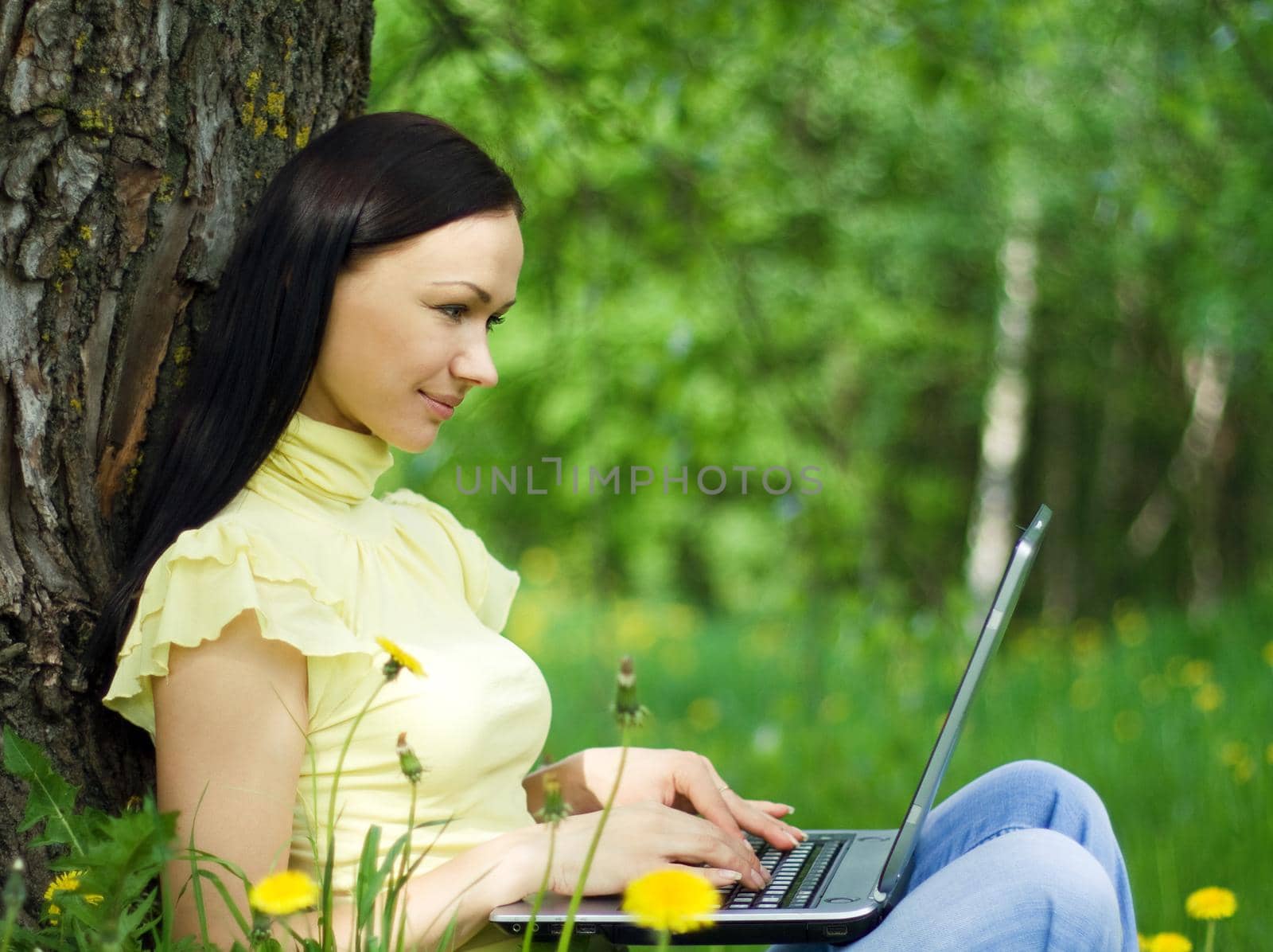 Young woman sitting on the grass with laptop on her knees.