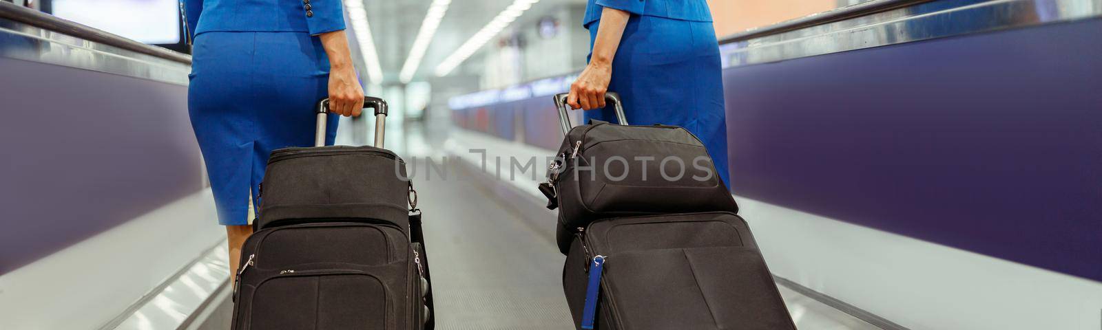Close up of woman stewardesses in air hostess uniform walking down airport terminal with trolley luggage bags