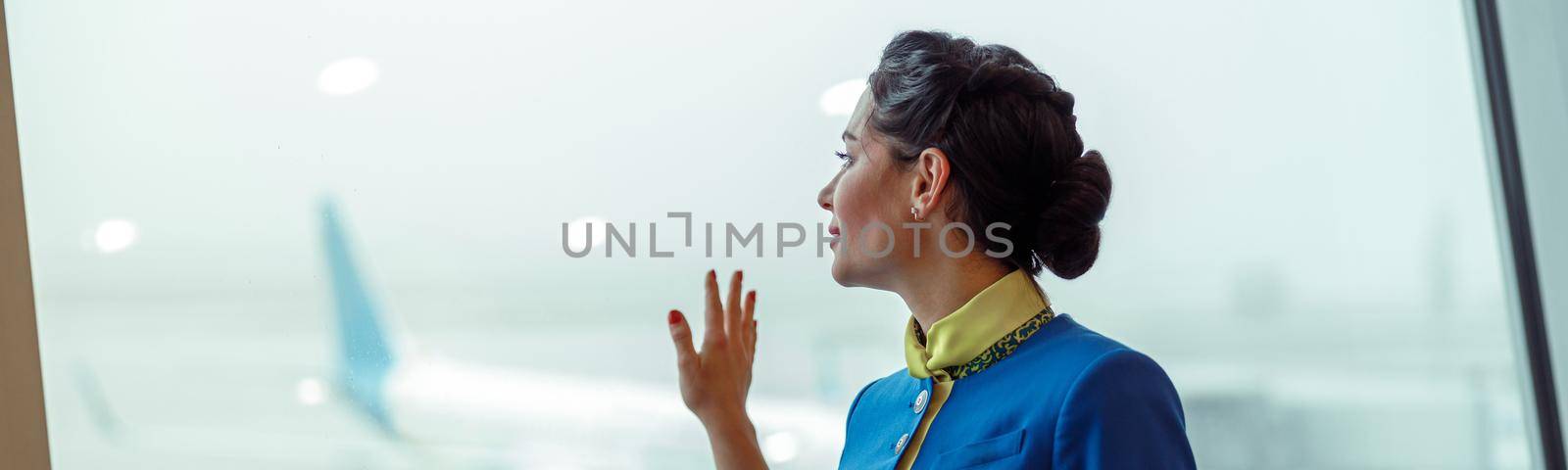 Woman stewardess placing hand on window in airport terminal by Yaroslav_astakhov