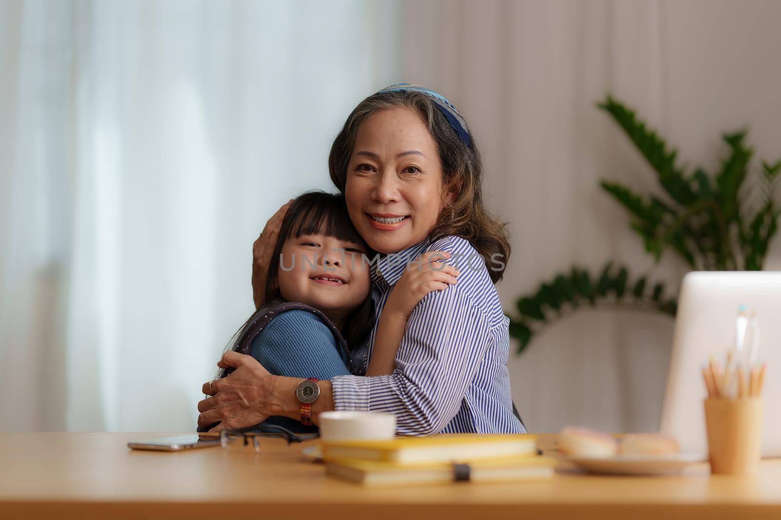 Happy moments of Granddaughter give hug while Asian senior business woman working at home. Family concept