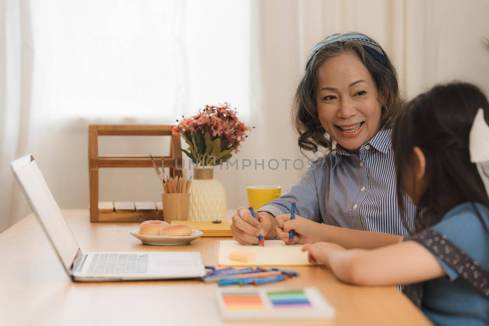 Happy moments of Asian grandmother with her granddaughter painting together at home. Leisure activities for children at home