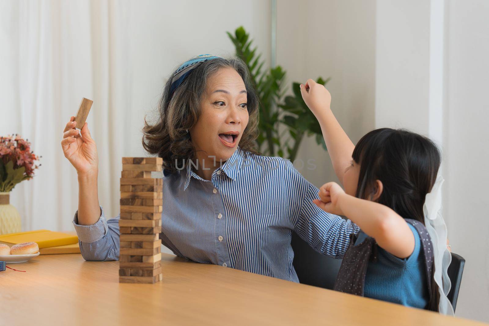 Happy moments of Asian grandmother with her granddaughter playing jenga constructor. Leisure activities for children at home. by itchaznong