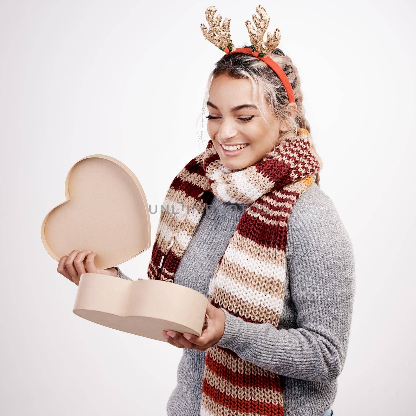 Whats in the box. Studio shot of an attractive young woman opening a heart-shaped boxed while dressed in Christmas-themed attire. by YuriArcurs