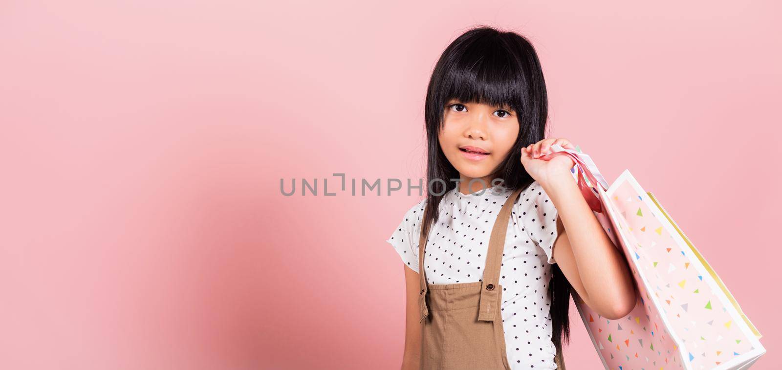 Asian little kid 10 years old smiling holding multicolor shopping bags in hands at studio shot isolated on pink background, Portrait of Happy child girl shopper lifestyle, Black friday concept