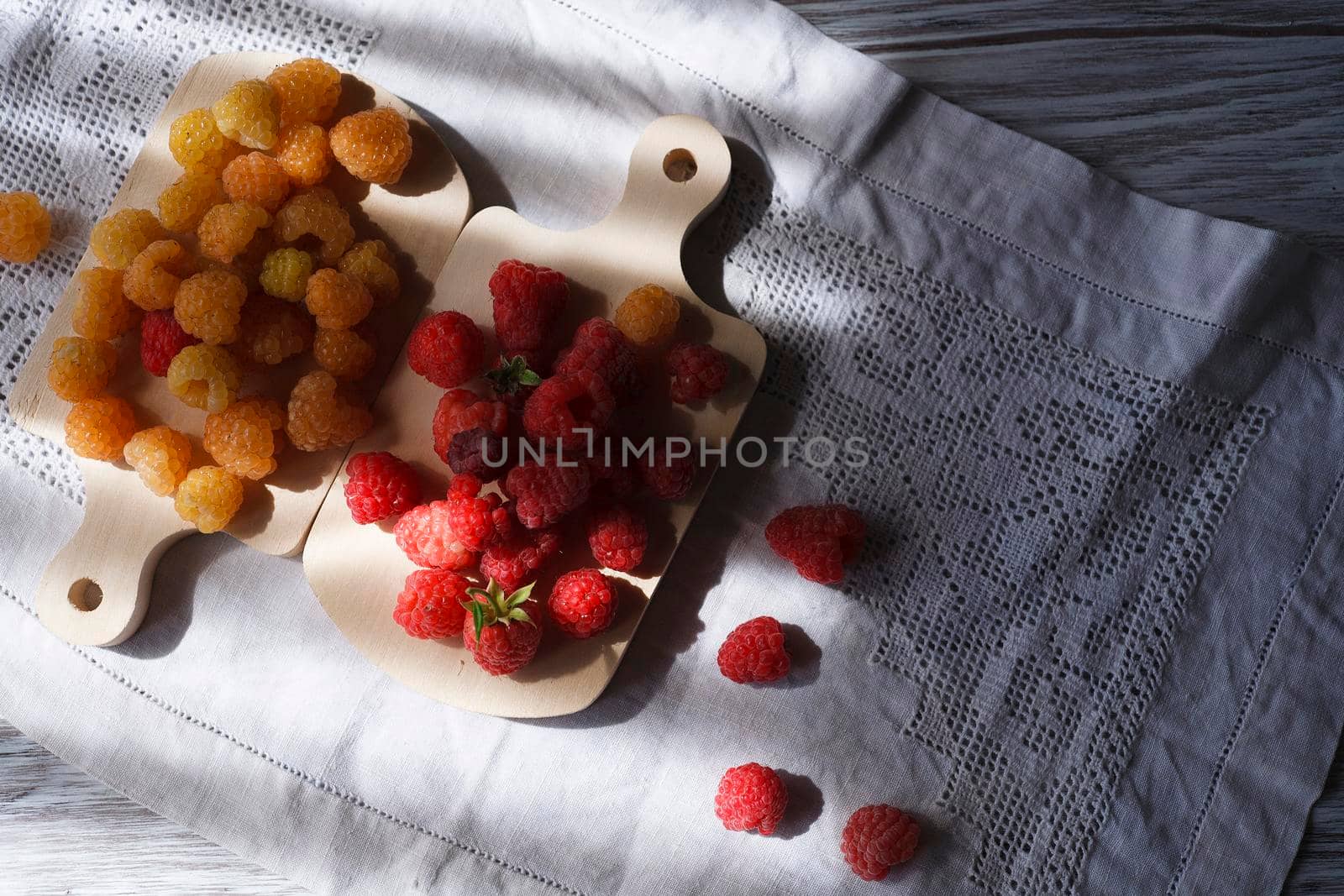 Two handfuls of fresh red and yellow raspberry on white wooden kitchen boards, sselectivew focus, hard light with copy space.