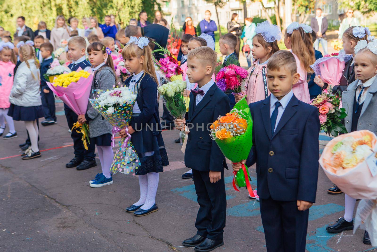 NOVOKUZNETSK, KEMEROVO REGION, RUSSIA - SEP, 1, 2021: Meeting with the first-grade pupils and teacher at schoolyard. The day of knowledge in Russia.