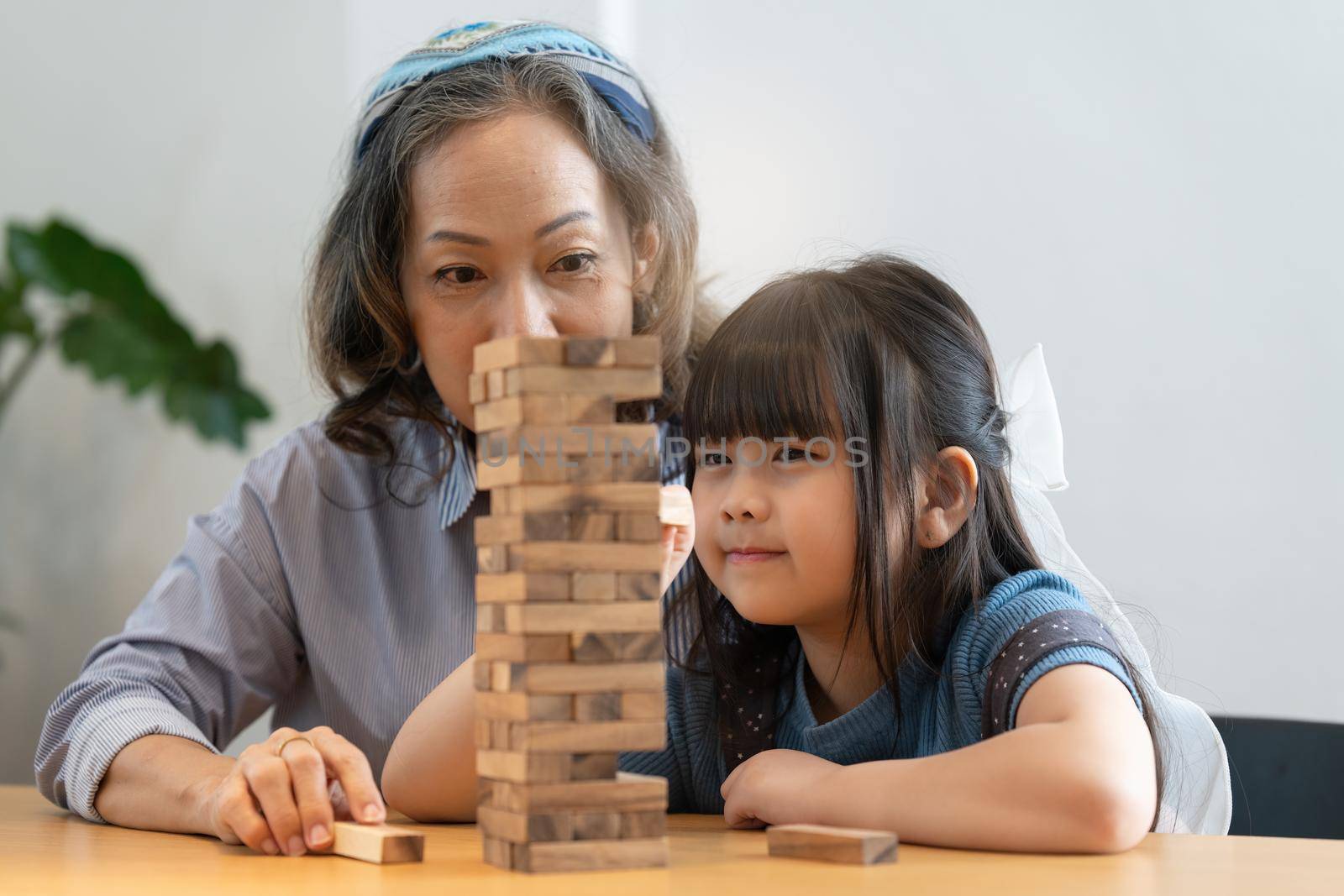 Happy moments of Asian grandmother with her granddaughter playing jenga constructor. Leisure activities for children at home. by itchaznong