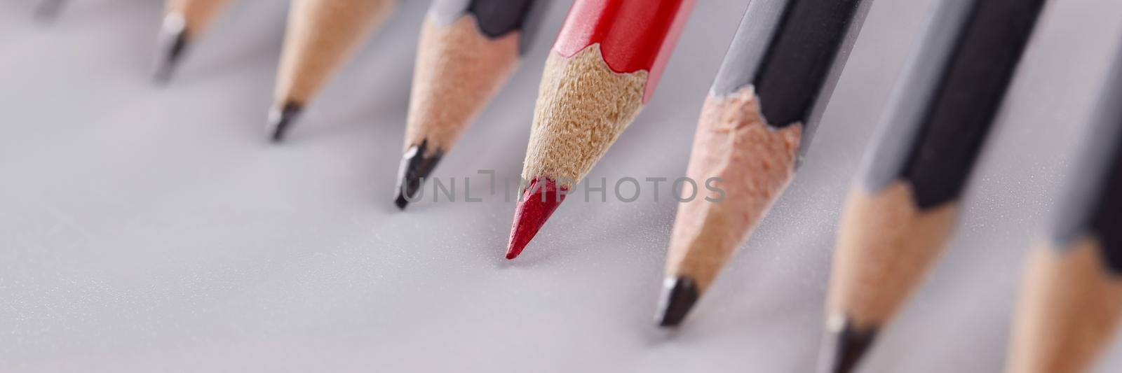 Red pencil that stands out from many identical black pencils on gray background by kuprevich