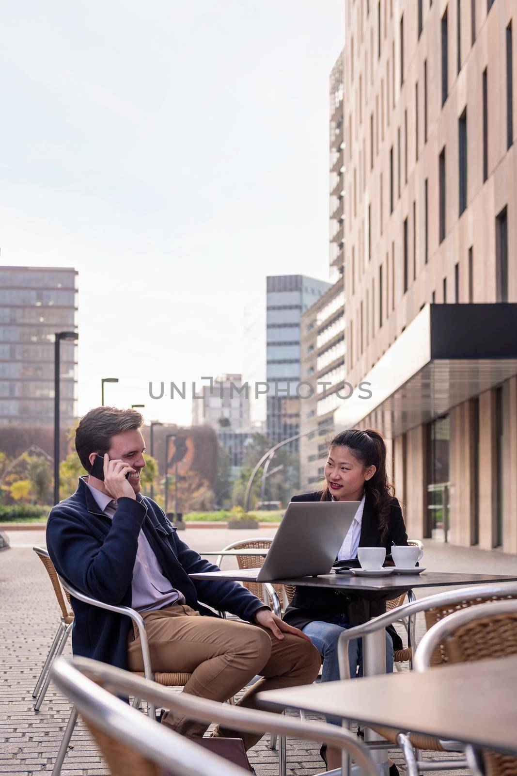 young businessman talking by phone while has a work meeting over coffee with his female partner on a terrace in the financial district, concept of entrepreneurship and business, copy space for text