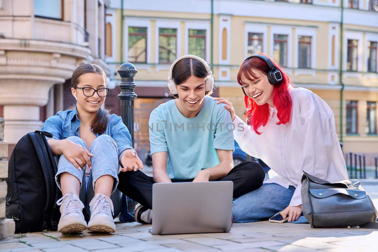 Teenage friends in headphones looking at a laptop by VH-studio