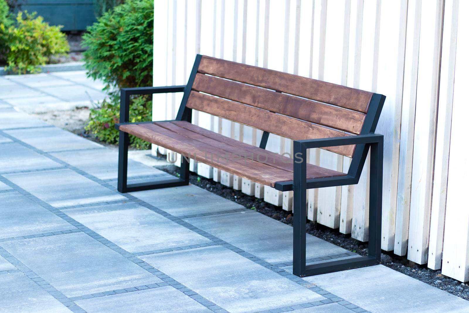 modern bench on the street on a summer day against the backdrop of green bushes. wooden bench in the courtyard of the business center. smoking area. High quality photo