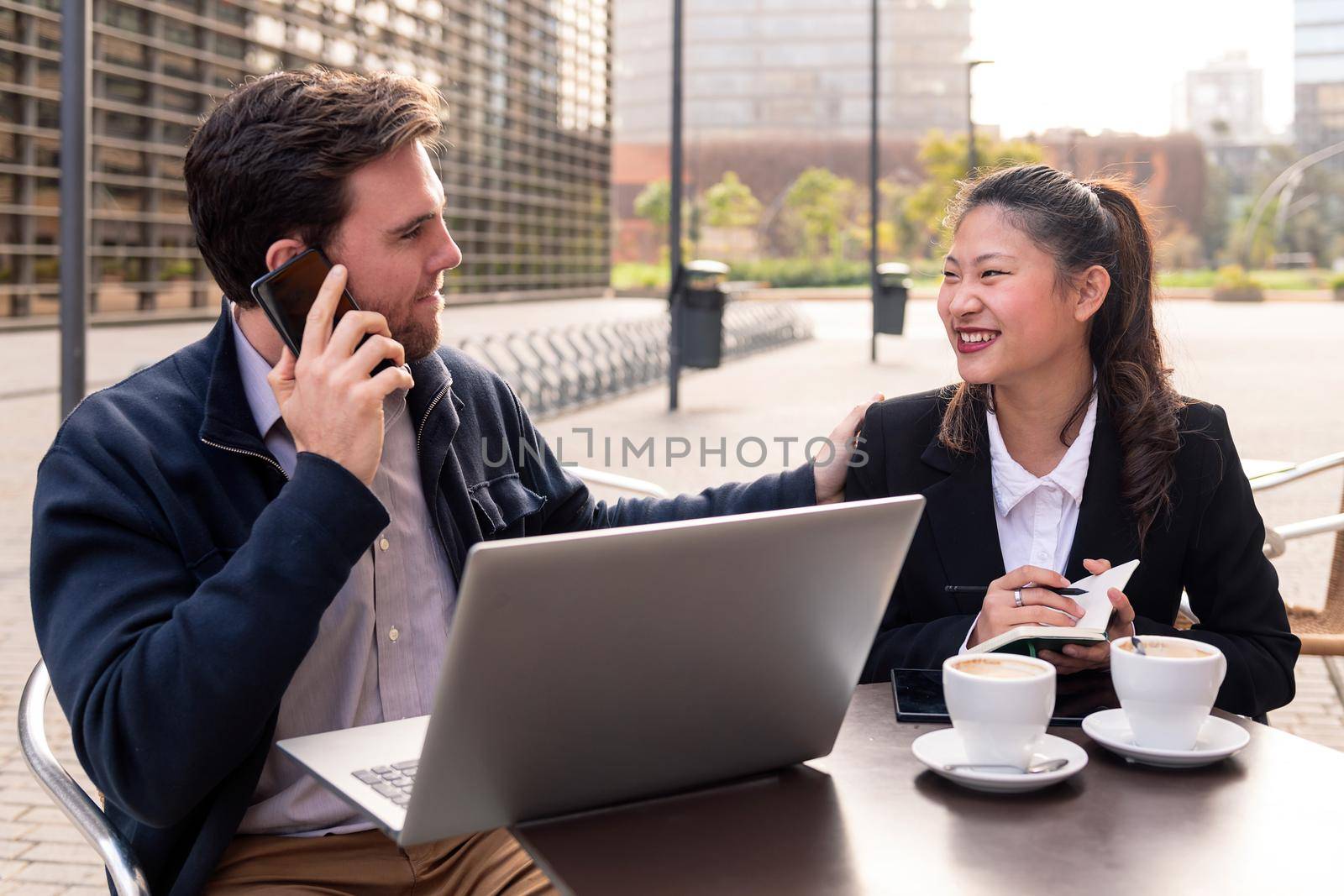 asian woman and caucasian man having a work meeting on the terrace of a coffee shop in the financial district, concept of entrepreneurship and business