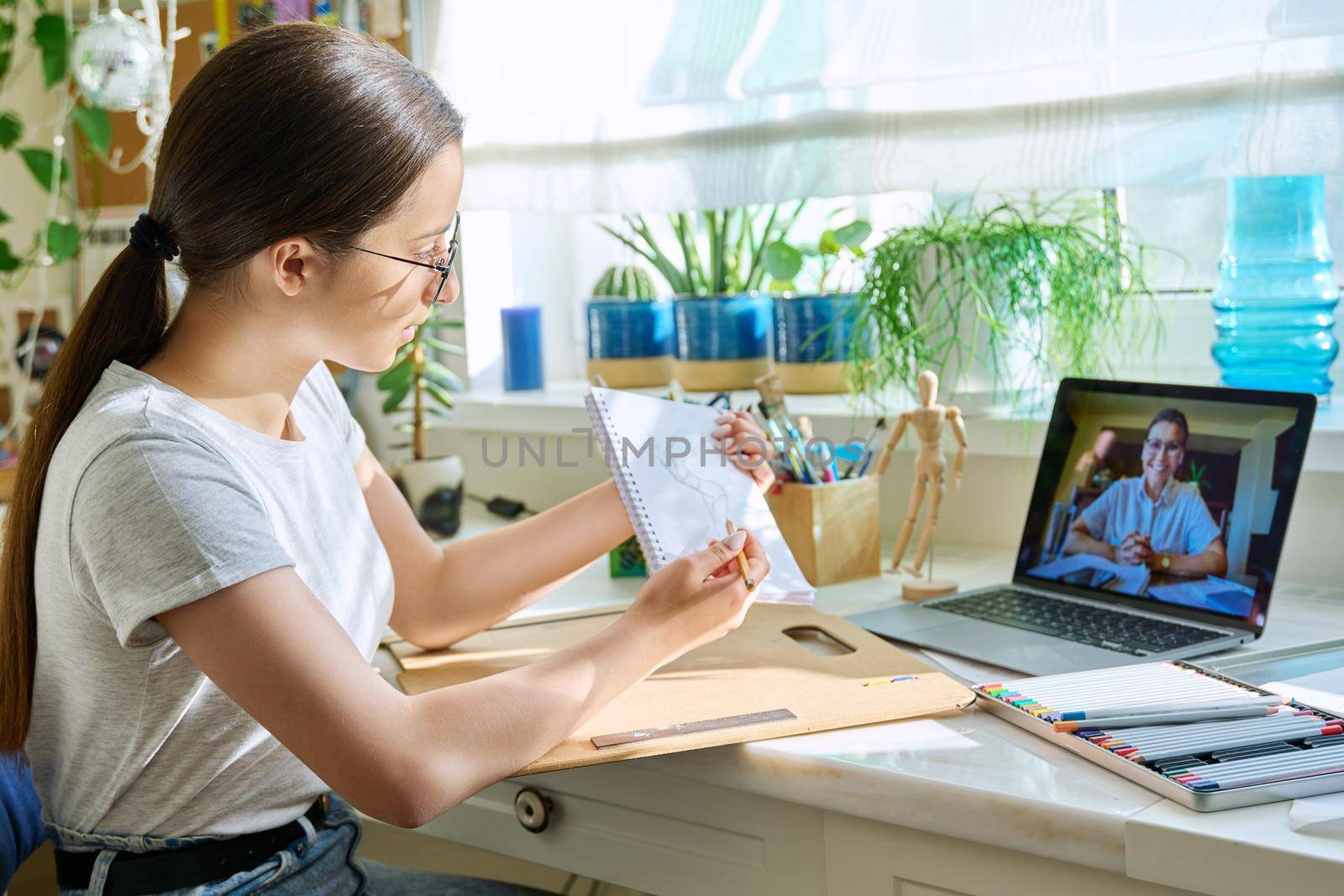 Online drawing lesson, teenage girl having video call conference chat with teacher sitting at table at home. Young creative art student. Creativity technology education e-learning adolescence concept