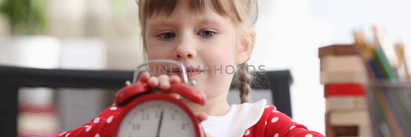 Portrait of cute child learn how to understand time and play with red retro clock. Curious look and interest in little childs eyes. Development concept