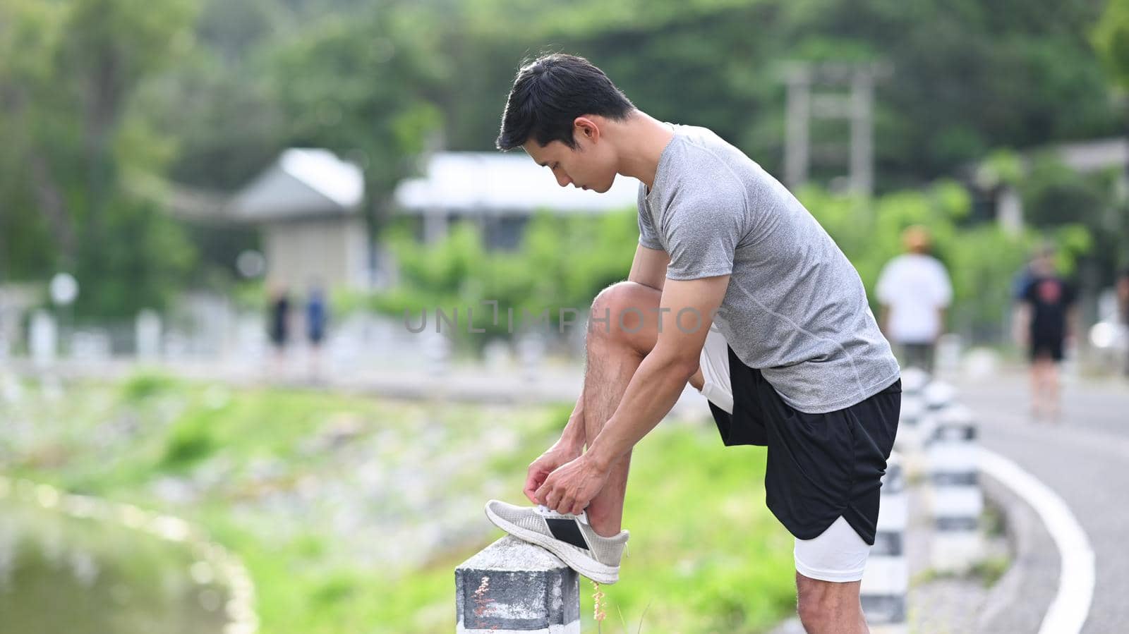 Athletic man tying shoelaces before running, getting ready for jogging outdoors. Healthy lifestyle, workout and wellness concept by prathanchorruangsak