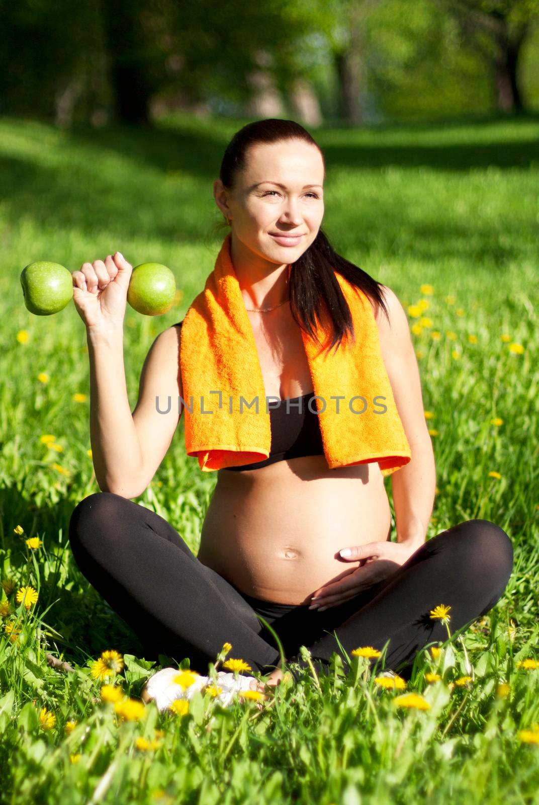 Pregnant woman with dumbbells and towel doing sports in the park.