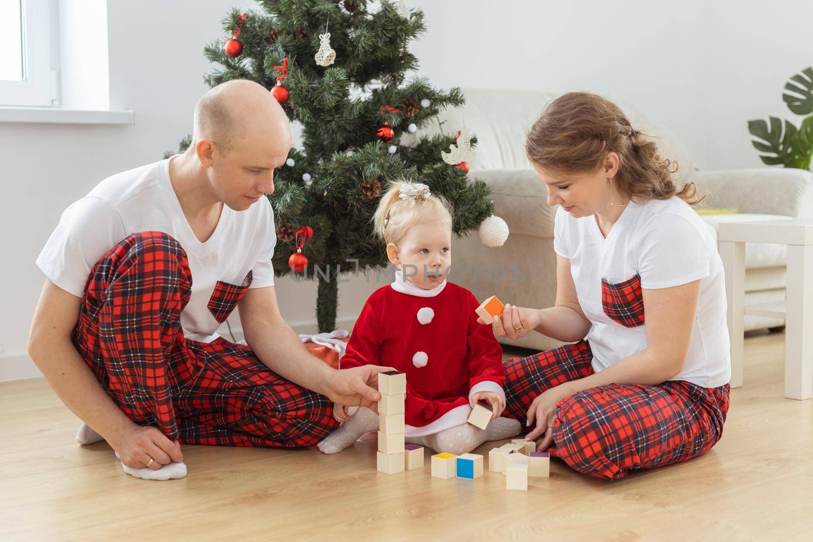 Toddler child with cochlear implant plays with parents under christmas tree - deafness and innovating medical technologies for hearing aid and diversity by Satura86