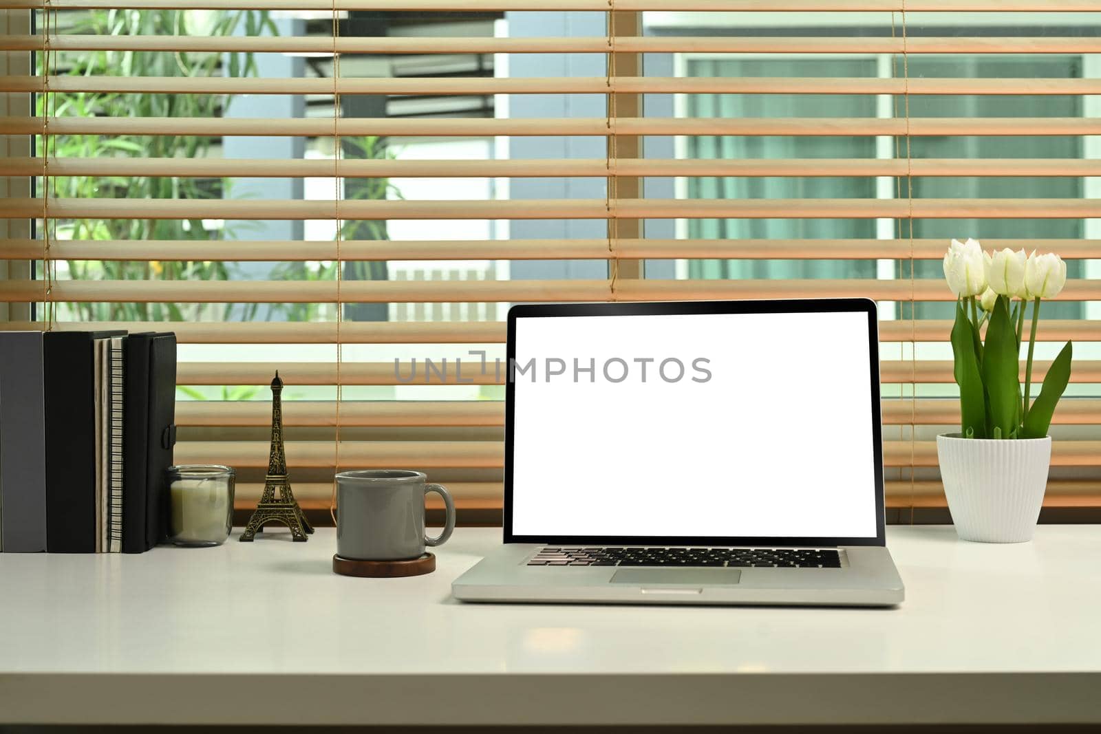 Computer laptop with white empty display, coffee cup, flower pot and books on home office desk by prathanchorruangsak