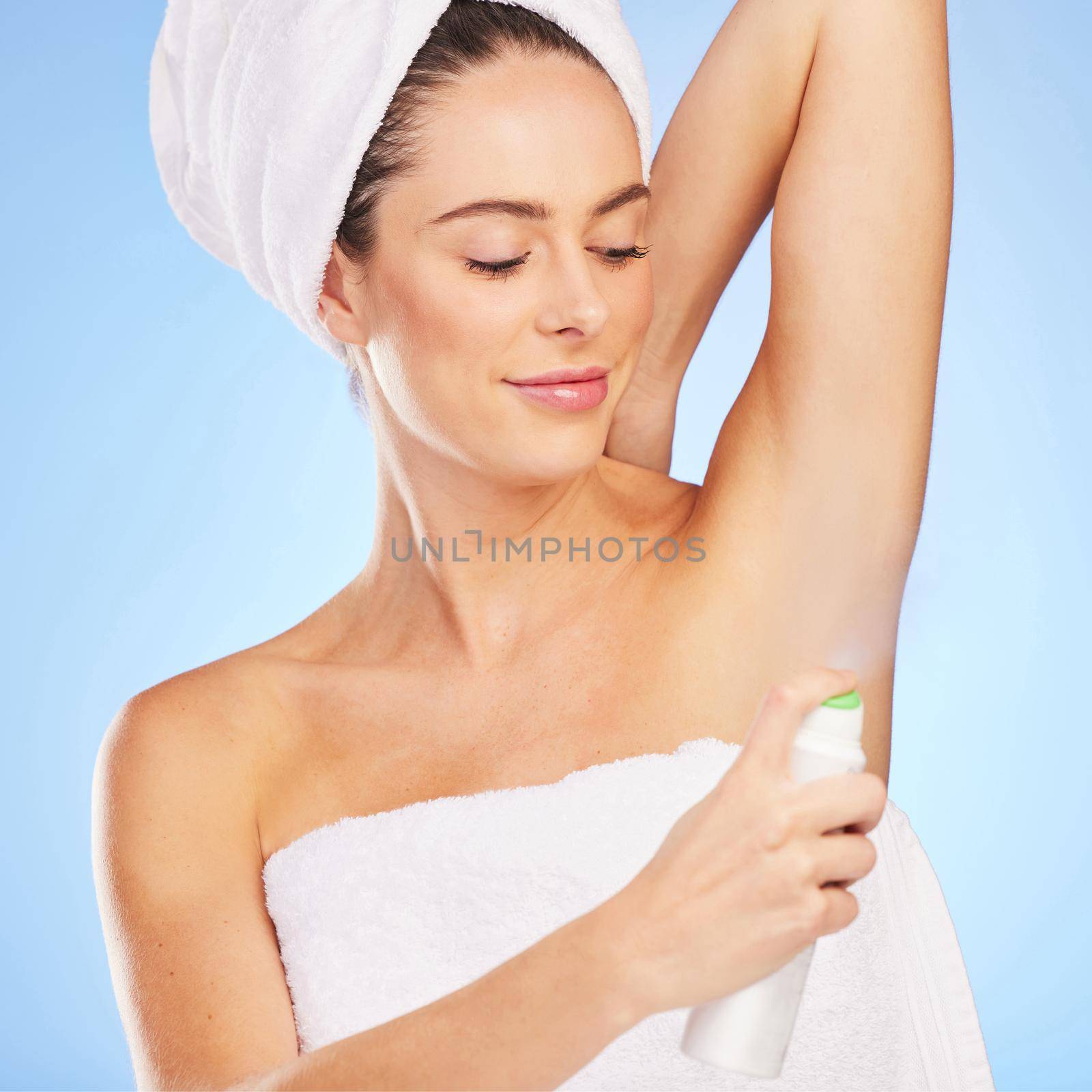 Have to keep myself fresh. Shot of a young woman applying deodorant against a blue background. by YuriArcurs