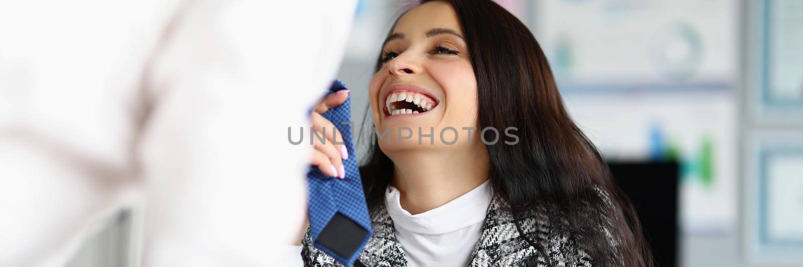 Businesswoman flirting with corporate male worker touching his tie and laughing by kuprevich