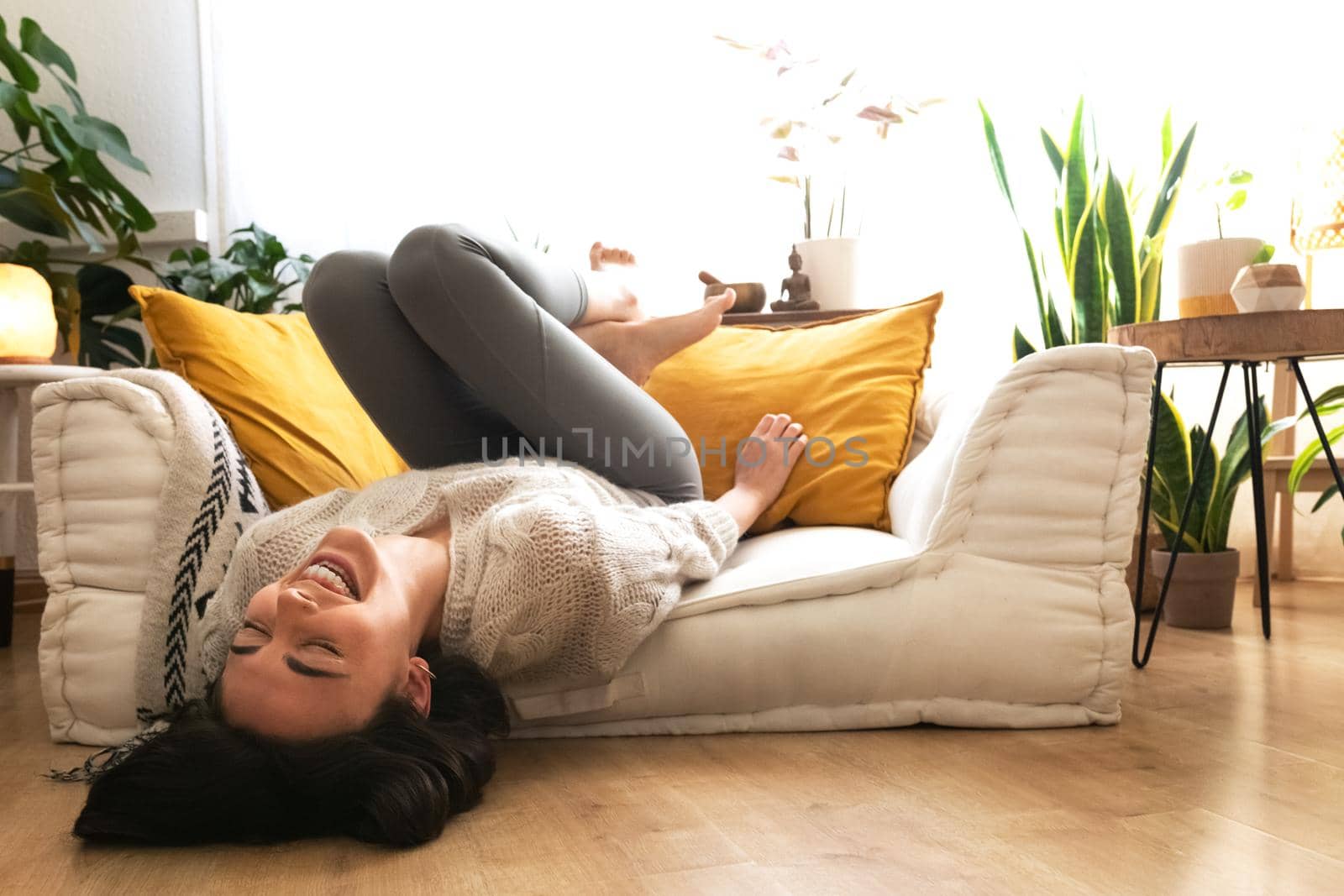 Young happy caucasian woman laughing out loud lying upside down on the sofa. Copy space. by Hoverstock