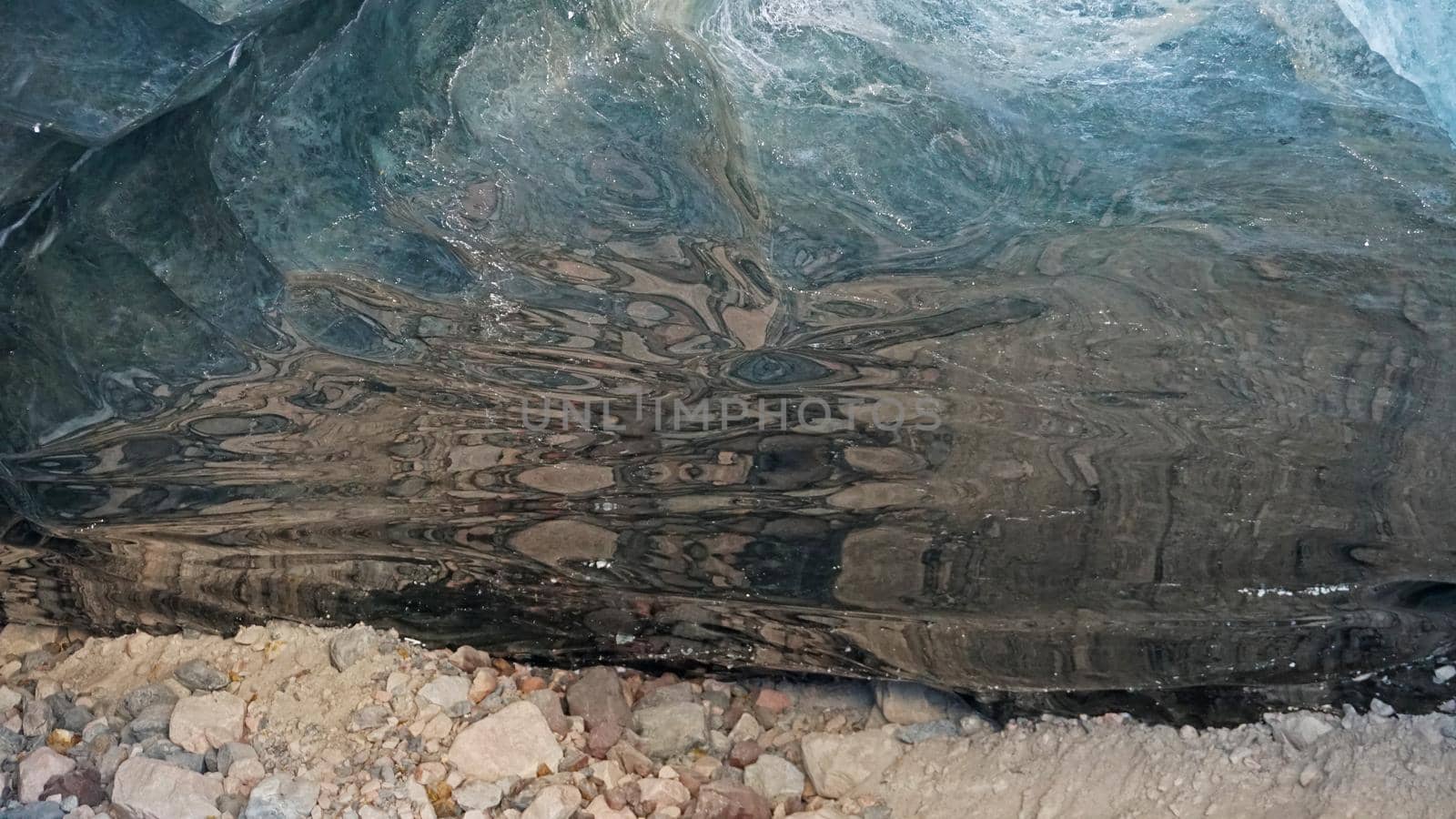 Ice cave in the snowy mountains. Tuyuk-Su glacier. Black ice reflects everything like a mirror. The ledge of stones collapsed. huge cracks in the ice tunnel. Snowy mountains of Almaty, Kazakhstan.