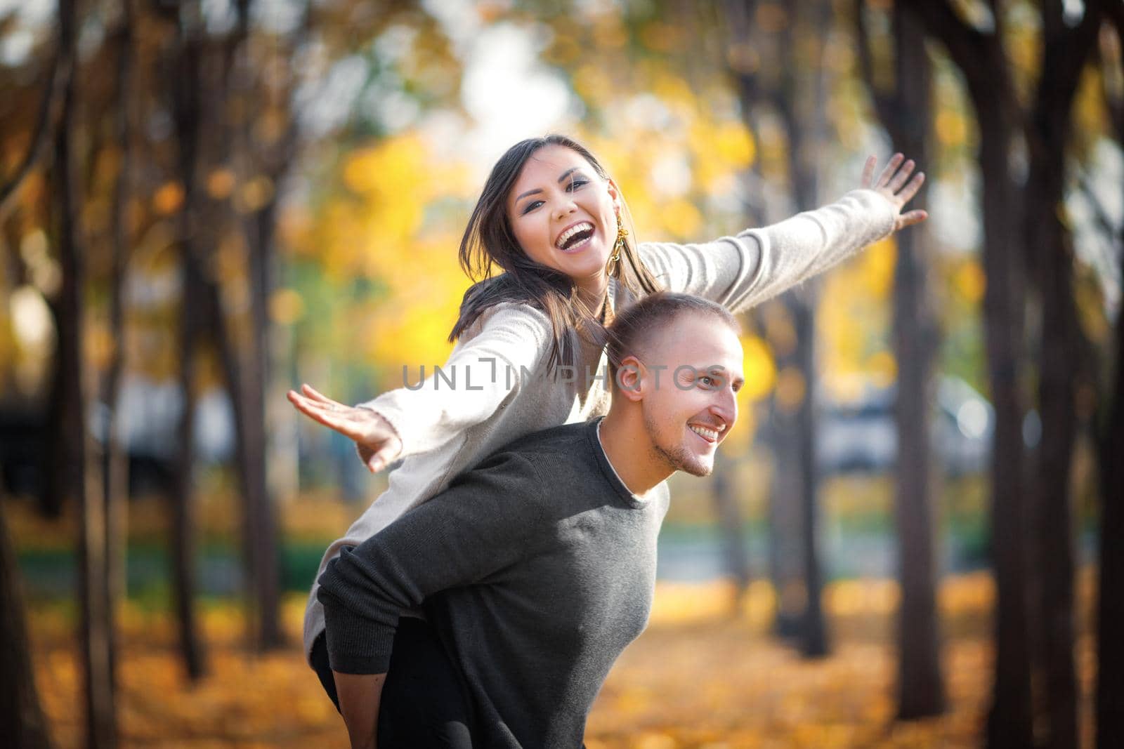 Enamoured young couple fool around in autumn outdoor. A man rolls a woman on his back, and she depicts a flight by Rom4ek