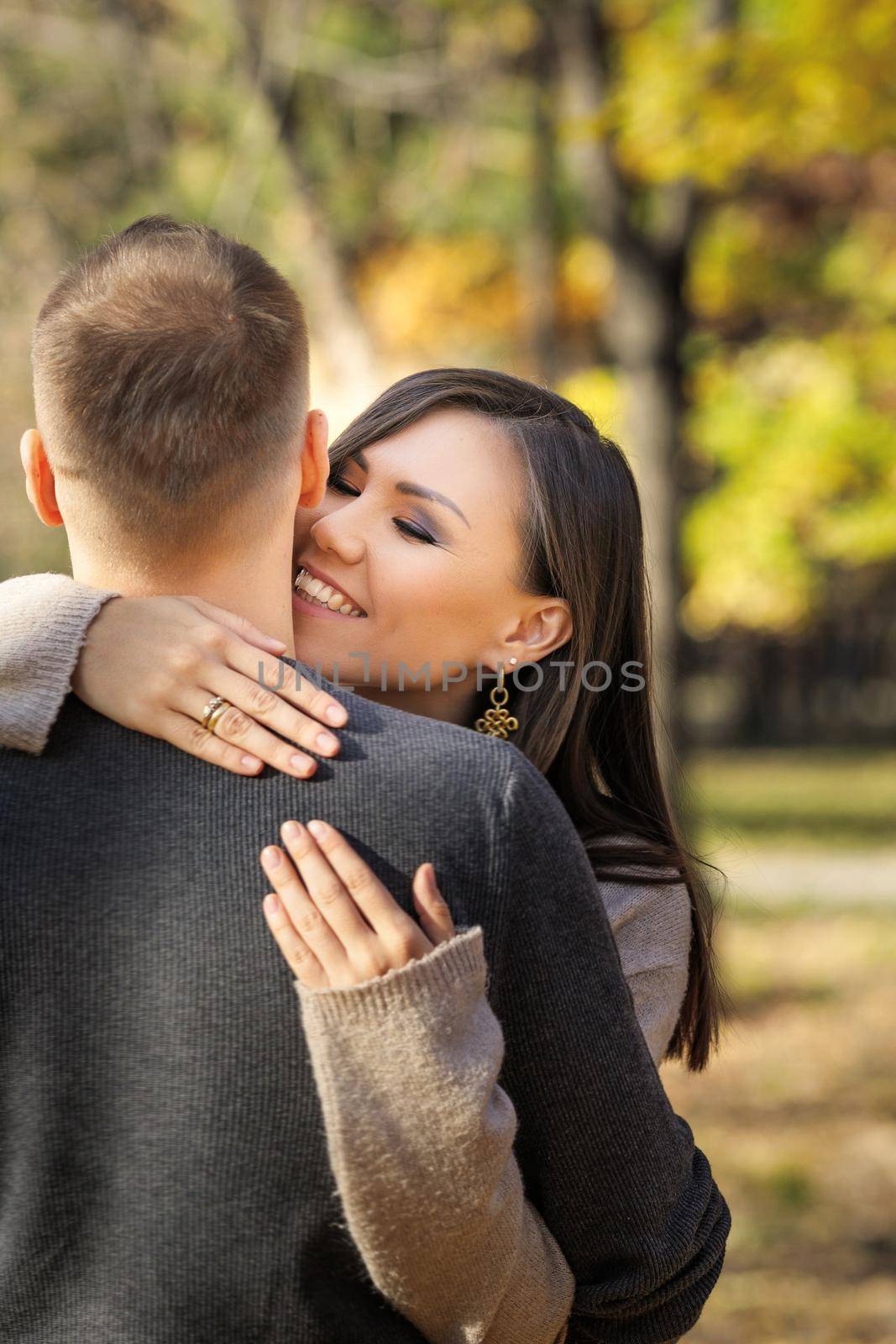 Beautiful young woman lovingly hugging her man in autumn park, vertical.