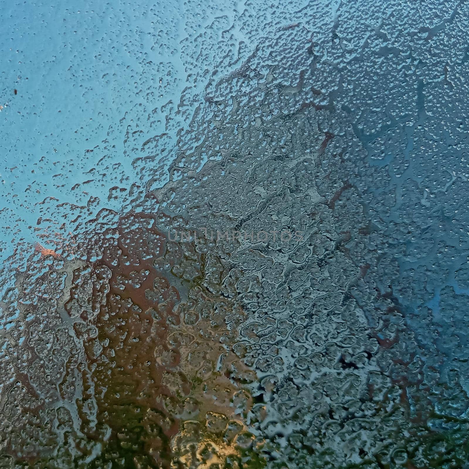 Frozen glass with the onset of cold weather. View through a layer of ice to the blue sky. Frost on the windshield, the rays of the morning sun melt the frost formed overnight. Background, texture.