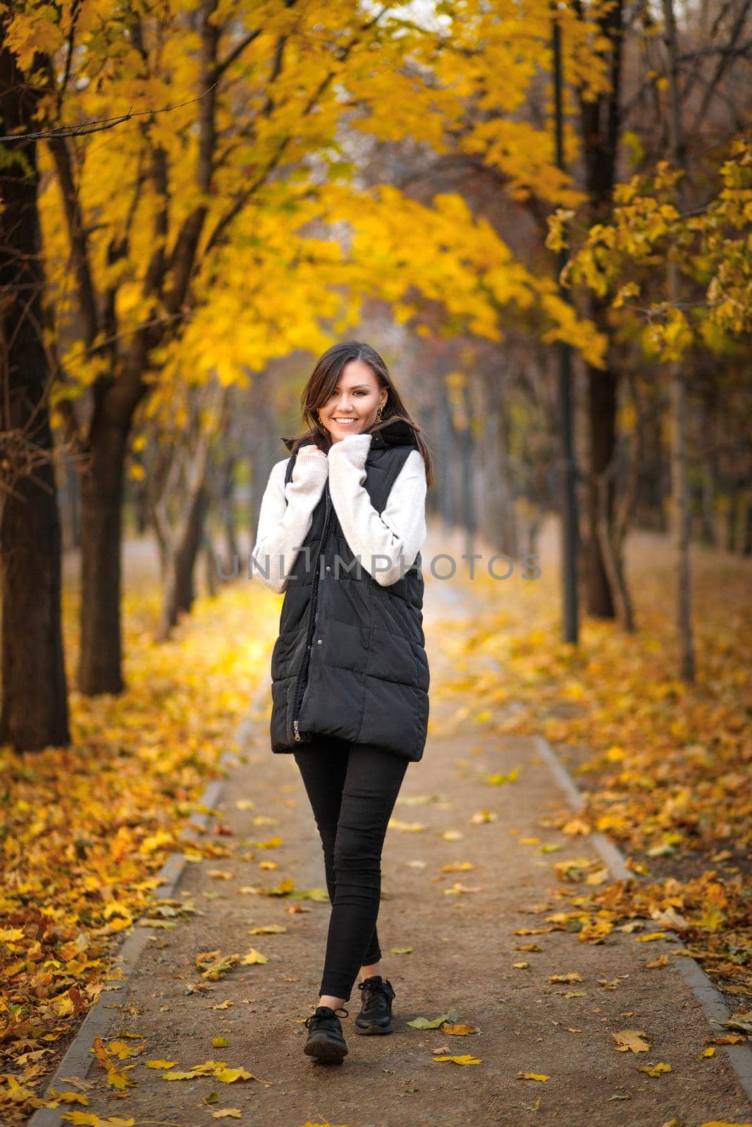 A young woman in autumn clothes walks in an autumn park with picturesque autumn foliage.