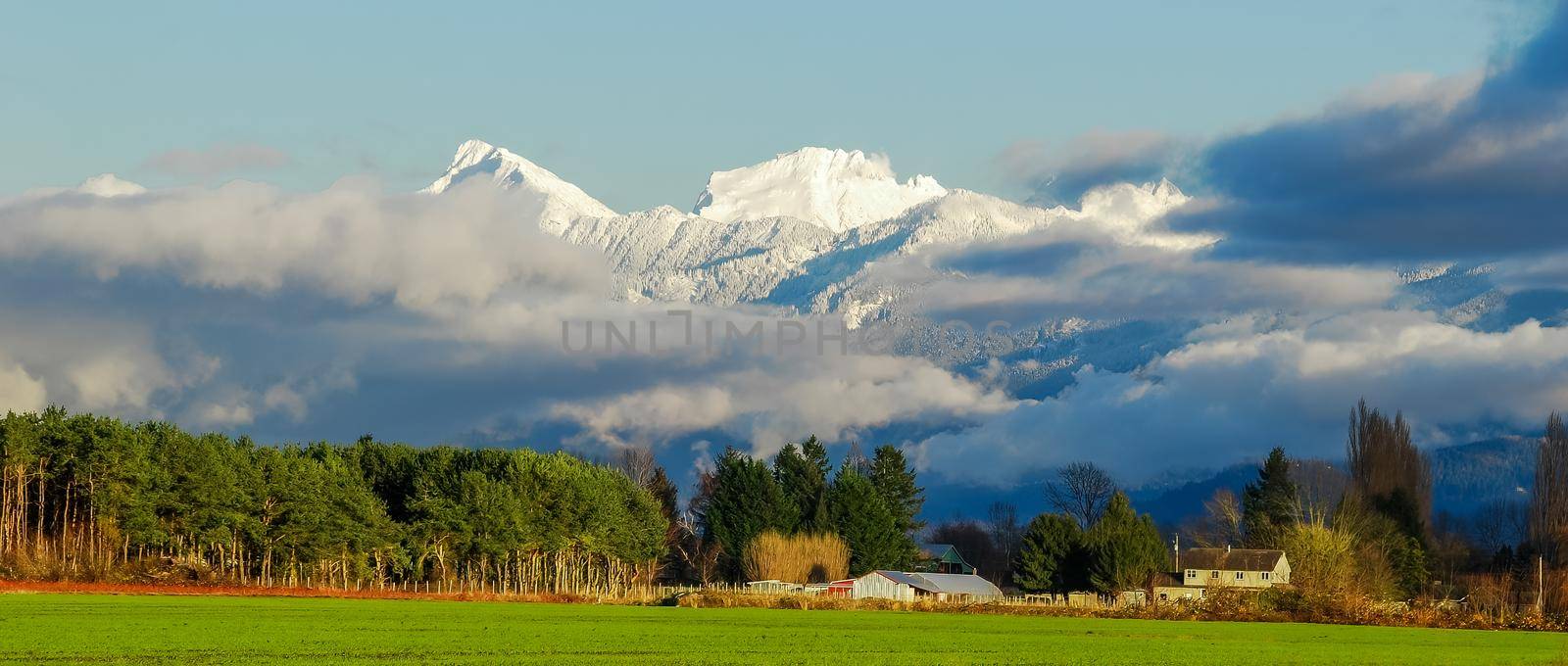 Pastoral overview over Fraser valley farm lands on snowy mountains background.