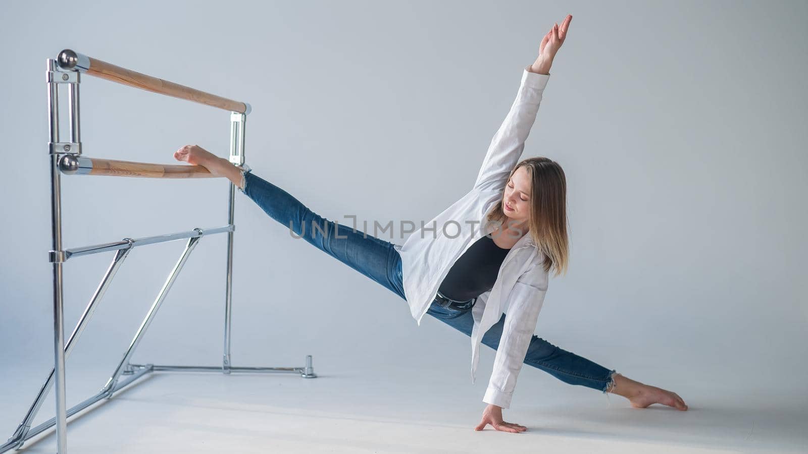 Caucasian woman in casual clothes pulls the split at the ballet barre. by mrwed54