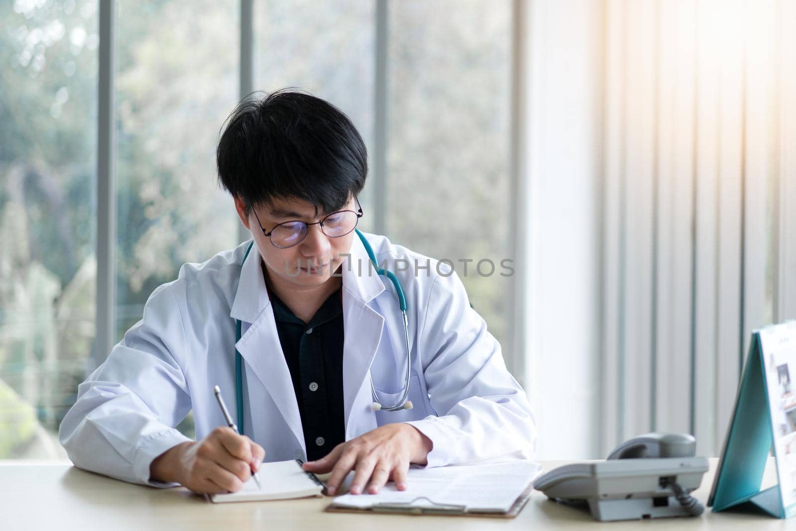 Male doctor sitting in office analyzing and writing patient sickness report by Buttus_casso