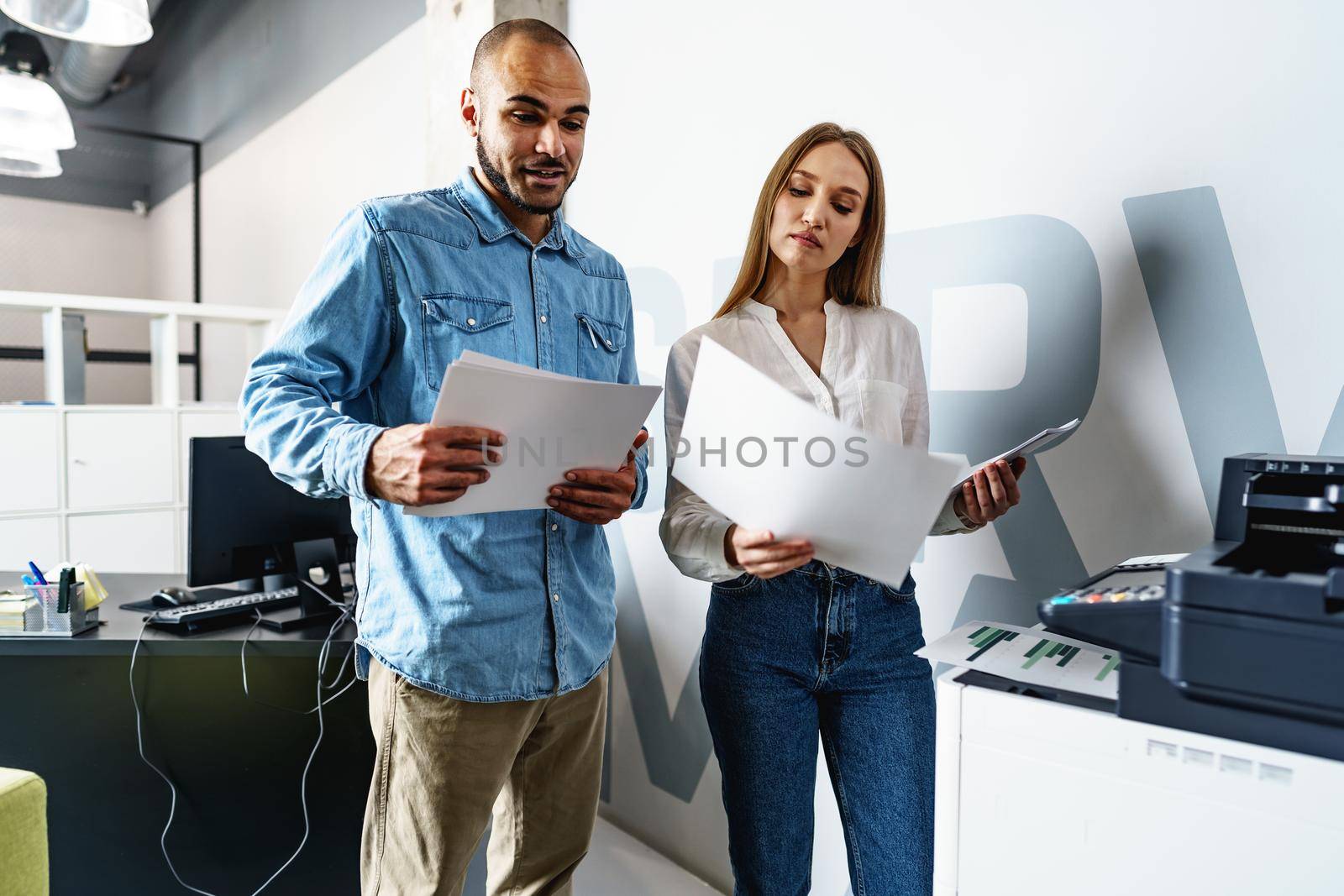 Two employees using new modern printer in office by Fabrikasimf