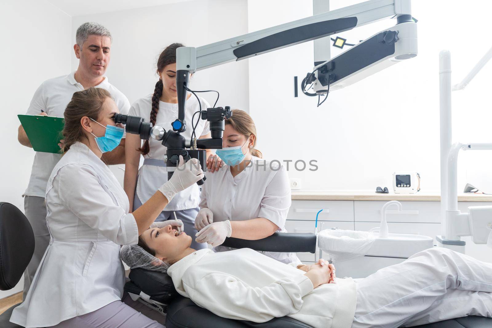 Group of students in dental clinic learn watching dental treatment with microscope