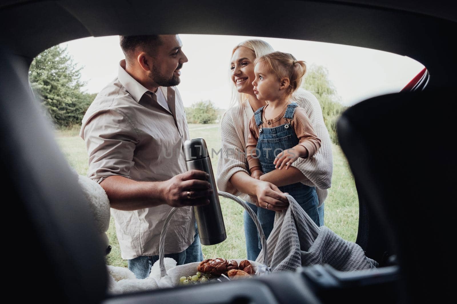 Young Family, Two Parents with Their Little Kid Preparing to Picnic Time Outdoors, View Through Open Trunk of SUV Car by Romvy