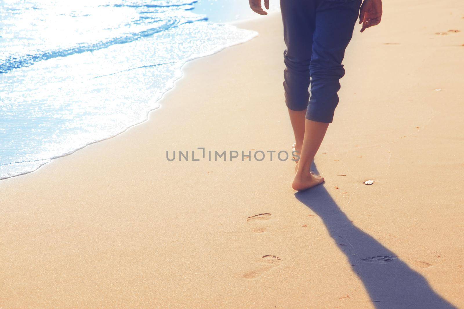 Walking on the beach, leaving footprints in the sand. by Taut