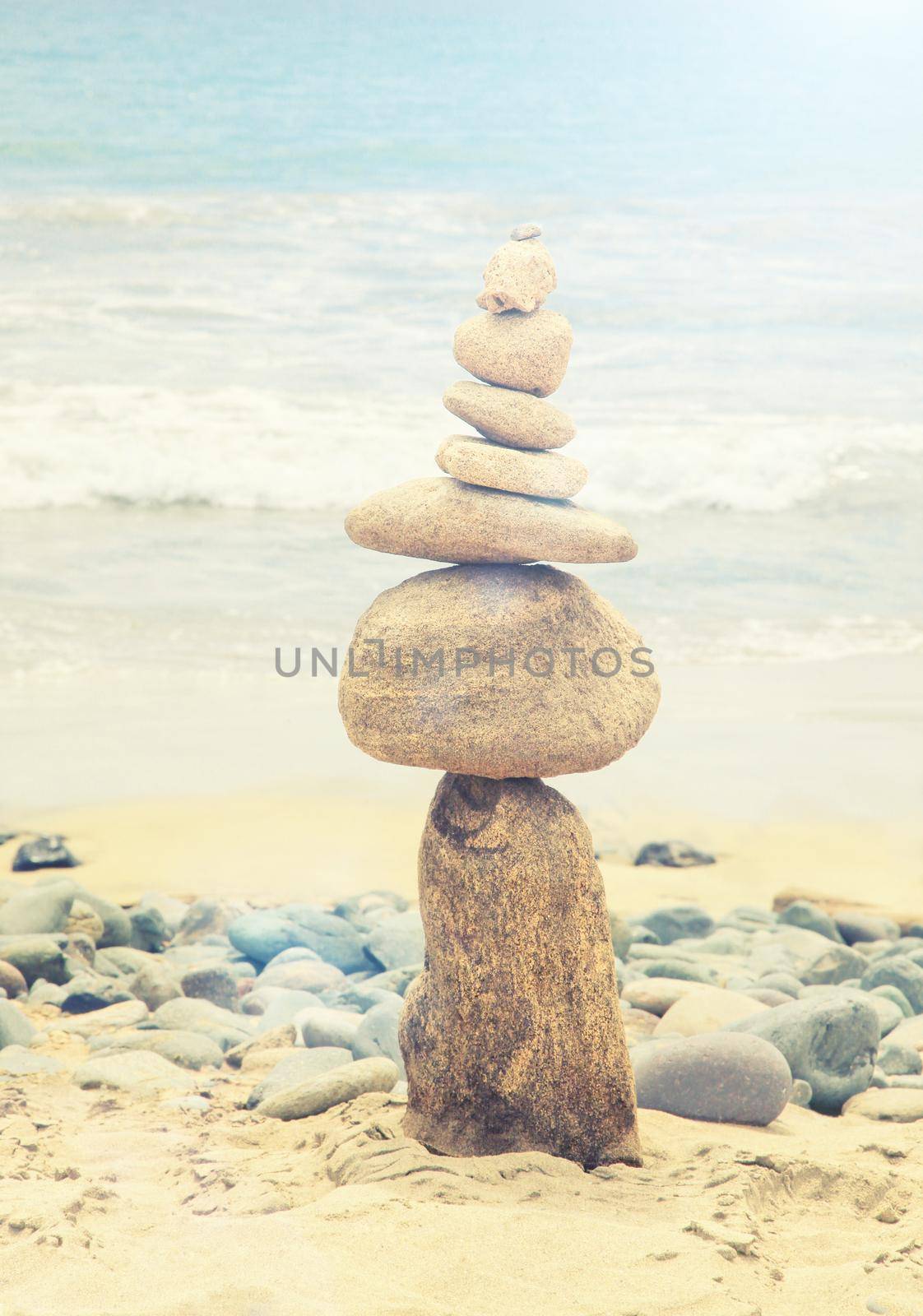 Balanced stones on a pebble beach during sunset. by Taut