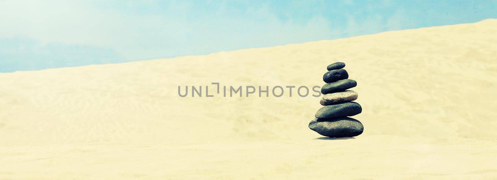 Balanced stones on a pebble beach during sunset. by Taut