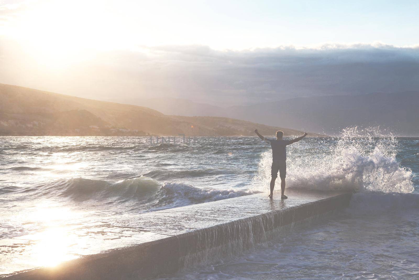 Feeling of freedom concept. Man standing on pier facing to the sea with big waves.