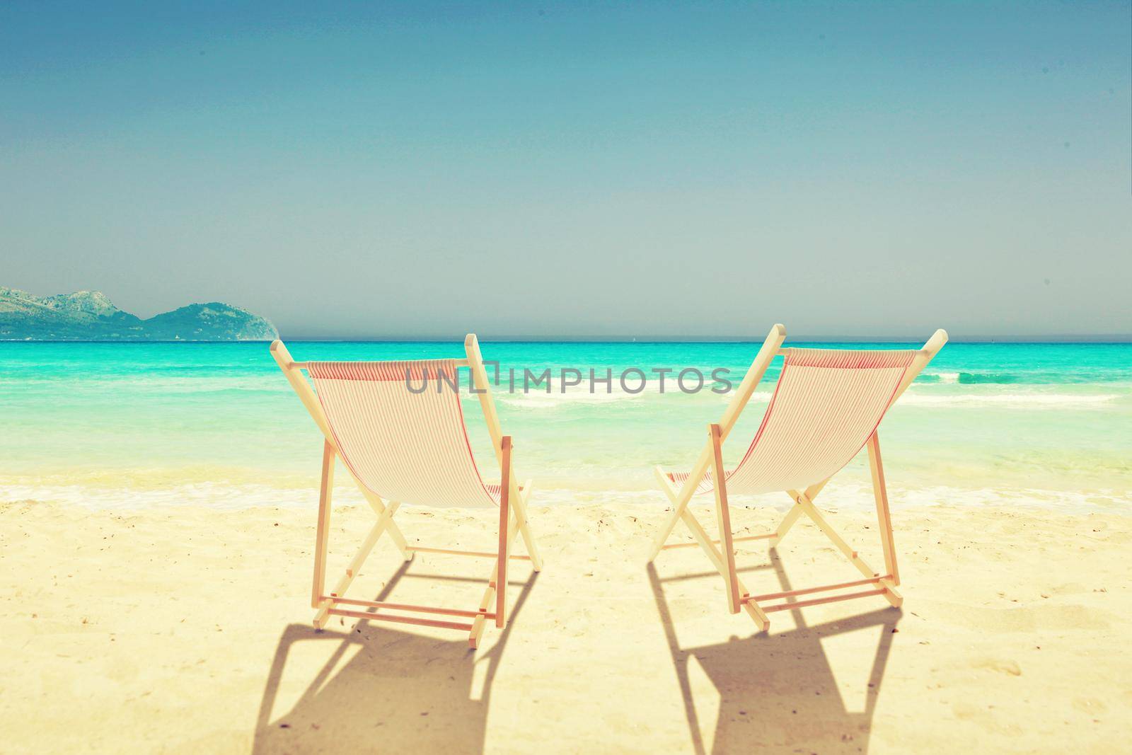 Wooden deck chairs on sandy beach near sea. Holiday background.