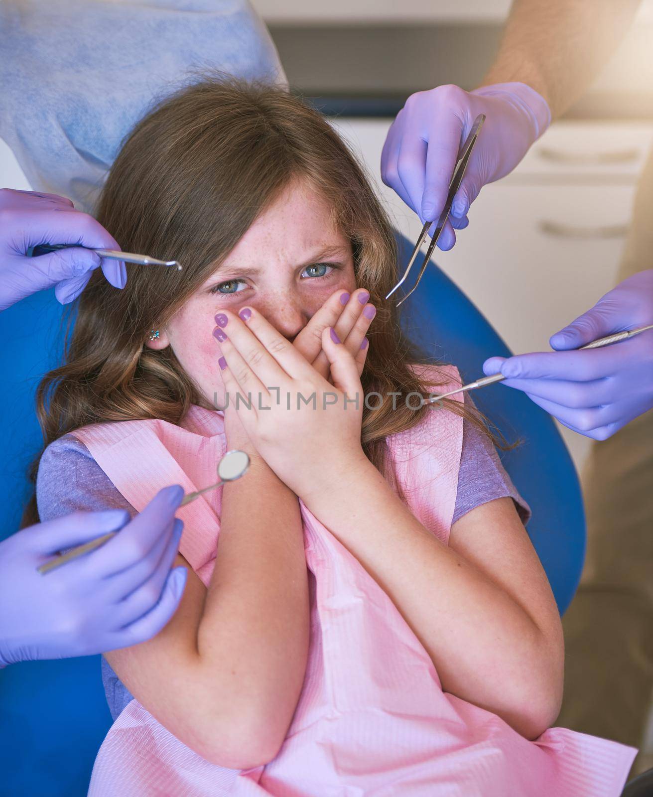 Childrens dental anxiety is very common. Shot of a little girl looking terrified as dentists get ready to examine her. by YuriArcurs