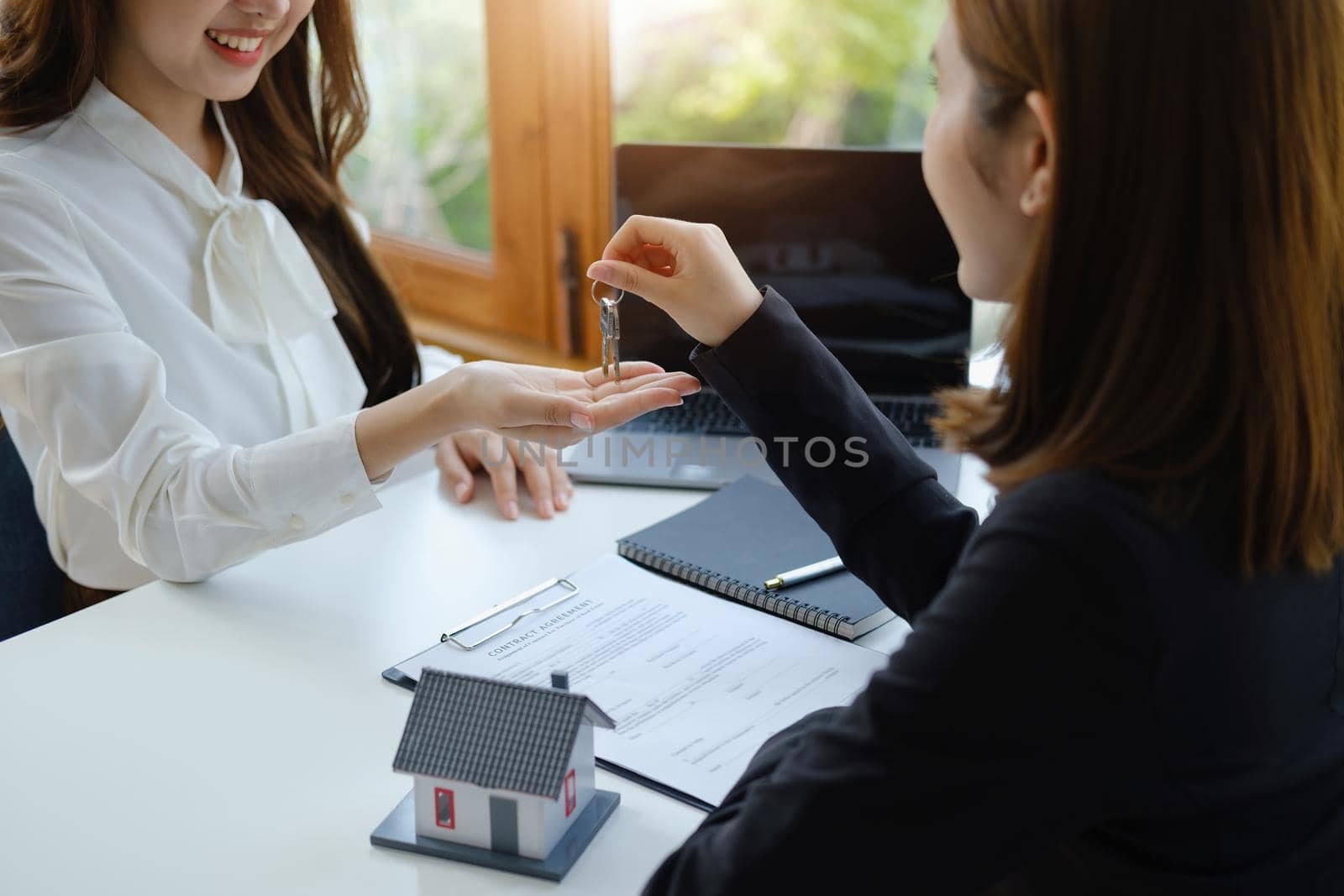 Accountant, businessman, real estate agent, Asian business woman handing keys to customers along with house after customers to sign by Manastrong