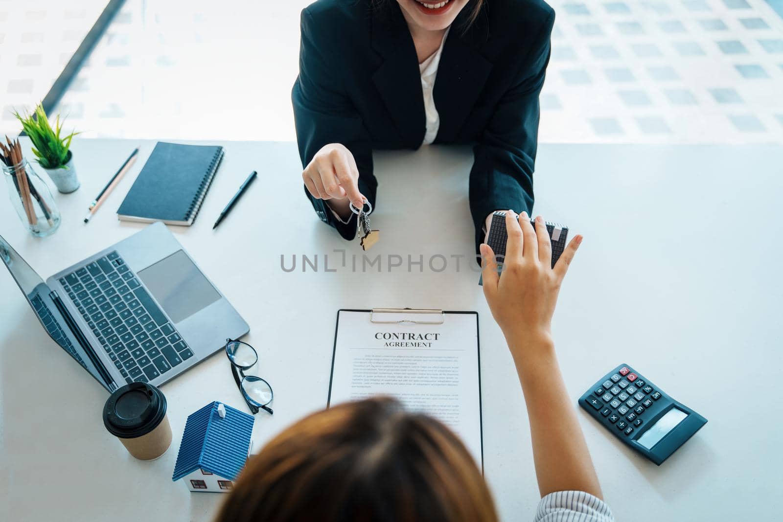 Accountant, businessman, real estate agent, Asian business woman handing keys to customers along with house after customers to sign by Manastrong