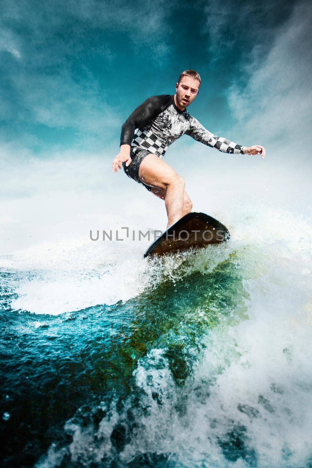 Surfing at blue sea. Young man balanced on wave on surfboard. Wake surf outdoor lifestyle.